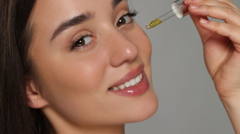Mulher latina e sorridente aplica um sérum facial de vitamina C após a limpeza de pele.