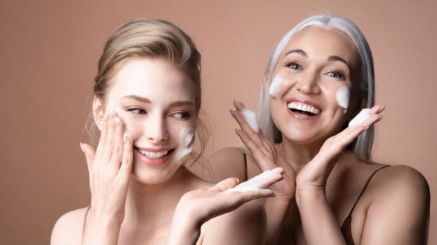 Mulher negra e feliz aplica o esfoliante para esfoliar o rosto com as duas mãos.