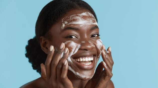 Mulher sorrindo passando sabonete facial no rosto com espumas.