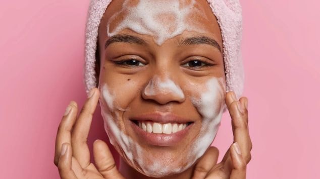 Jovem aplica sabonete ou gel de limpeza para limpar a pele do rosto em sua skincare.