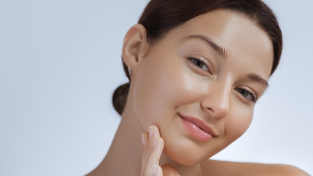 Mulher com pele radiante e uniforme, sorriso leve e expressão tranquila, tocando suavemente o rosto após rotina de skincare com Sérum de Limpeza Iluminador.