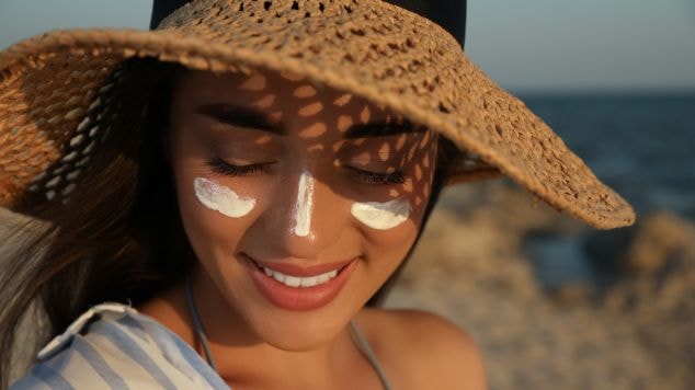 Jovem mulher aplica protetor solar facial em spray e em creme para garantir a proteção solar.