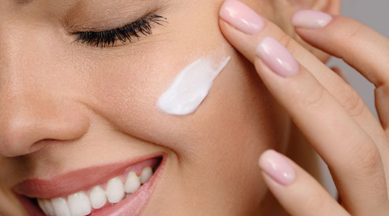 Mulher jovem e sorridente aplica um hidratante facial em sua pele do rosto