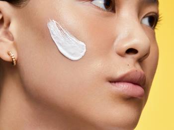 Perfil de jovem com um swatch de creme de limpeza na bochecha, exibindo a textura suave do produto sobre a pele limpa e hidratada.
